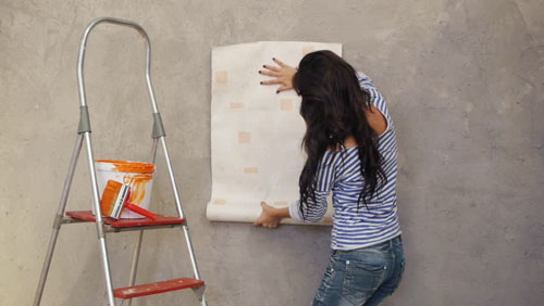 Young woman holding up wallpaper to wall