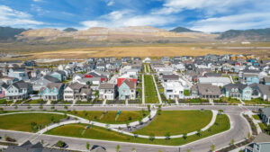 Aerial view of the Daybreak suburban neighborhood, where houses and green lawns stretch towards mountains under a blue sky, embodying the charm of the Contempo Collection.