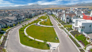 Aerial view of a suburban neighborhood from the Daybreak Contempo Collection, showcasing curved streets, green spaces, and modern homes under a blue sky.