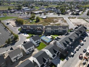 Aerial view of a residential neighborhood with rows of townhouses, a central pool area, parked cars, and surrounding open spaces.