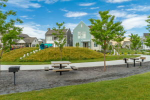 A picturesque park with picnic tables and trees, set against a backdrop of residential homes, lies under the clear blue sky of Daybreak.