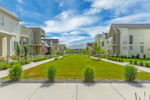 A suburban neighborhood from the Contempo Collection, showcasing modern houses and manicured lawns, unfolds along a central pathway under a daybreak sky dotted with clouds.