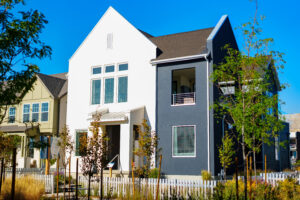 This exquisite two-story home from the Contempo Collection features a sleek white and dark gray exterior. Situated in the charming neighborhood of Daybreak, it boasts front yard trees and a classic white picket fence, offering both modern design and timeless appeal.