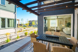 At daybreak, the outdoor patio with wicker chairs from the Contempo Collection encircles a table, all beneath a pergola. Through the glass doors, there's a glimpse into the modern living room.