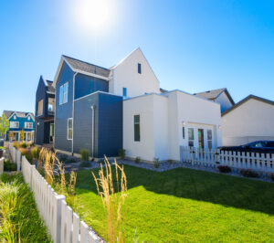 Modern house from the Contempo Collection with a striking white and dark blue exterior, set against a bright daybreak sky, framed by a neatly trimmed lawn and a classic white fence.