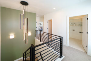 Modern hallway with a black metal railing, green accent wall, and geometric pendant light fixture from the Contempo Collection offers a fresh start like daybreak, infusing the space with contemporary elegance and a hint of early morning serenity.