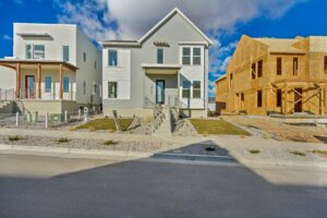 Three modern houses under a blue sky, one with a light gray facade, another still under construction with wooden frames, and a white house with a brown accent.