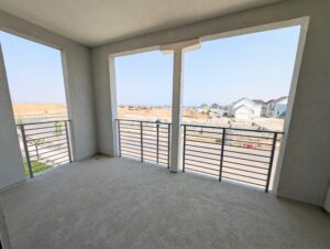 A covered balcony with a metal railing offers a scenic vista of a quaint street and charming houses beneath the clear blue skies of Cascade Village.