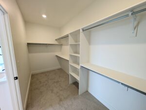 A spacious empty walk-in closet, reminiscent of the elegance found in Cascade Village, features white shelves, hanging rods, and a carpeted floor.