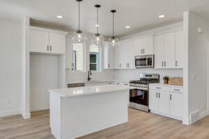 Modern kitchen with white cabinets, island, and stainless steel appliances. Three pendant lights hang above the island, and wood flooring is visible.