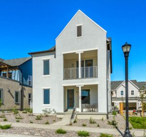 A row of modern suburban houses with stone walkways and a streetlamp against a clear blue sky.