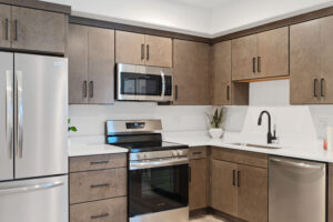 Modern kitchen with stainless steel appliances, brown cabinets, and a white countertop in the heart of Cascade Village.