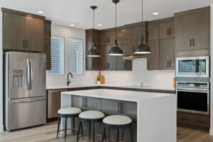 Located in the heart of Cascade Village, this modern kitchen boasts wooden cabinets, stainless steel appliances, an island with stools, and elegant pendant lighting—a perfect blend of style and legacy for any culinary enthusiast.