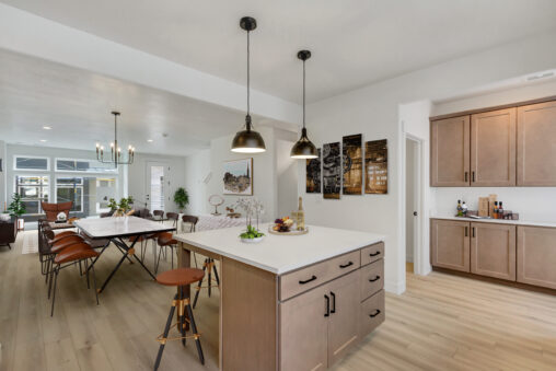 Modern open-concept kitchen and dining area featuring a central island with pendant lighting, a long dining table with wooden chairs, minimalist decor, and light wood flooring.