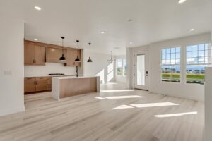 Bright, empty open-concept kitchen and living area with wooden floors, modern lighting fixtures, and large windows overlooking a scenic view.