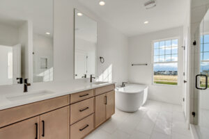 Modern bathroom with a large mirror, dual sinks, standalone bathtub, and a window with a scenic view.