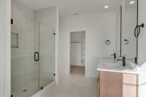 Modern bathroom with a glass-enclosed shower, dual sinks with mirrors, and a doorway leading to a walk-in closet.