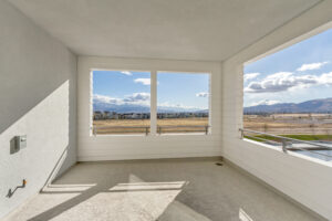 A spacious empty balcony with open windows overlooks a scenic view of mountains and an open field under a cloudy sky.