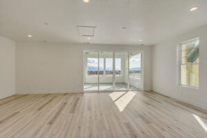 Empty room with light wood flooring, white walls, recessed lighting, and large windows leading to a balcony with a scenic mountain view.