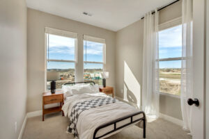 A minimalist bedroom with a single bed and wooden side tables, nestled in the basement. Through two windows, the view unfolds to a bustling construction site outside.