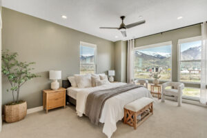 Envision a modern bedroom with a large bed, green walls, and stunning mountain views through expansive windows. As part of a comprehensive home renovation project, this sanctuary features beige carpeting and minimal decor, showcasing the transformation from an underutilized basement space.