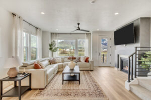 A modern living room with an L-shaped sofa, fireplace, and large windows showcasing stunning mountain views. The neutral tones and cozy decor create an inviting ambiance. Enhanced with the efficiency of ML+, this space offers a seamless blend of contemporary aesthetics.