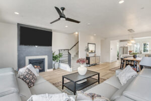 Modern living room with gray sofas, a fireplace, wall-mounted TV, and an adjacent dining area with a chandelier. This stunning space exemplifies home improvement at its finest, offering both style and functionality that elevates everyday living.