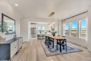 Modern dining area with a wooden table, black chairs, and a blue rug, adjacent to a kitchen boasting stainless steel appliances and integrated home automation features. Consider basement remodeling to extend this sleek style underground.