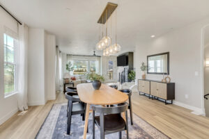 The modern dining area, nestled in a stylish basement, features a wooden table, black chairs, pendant lights, and large windows. With neutral decor and a cozy ambiance, it's an ML+ setting for memorable gatherings.