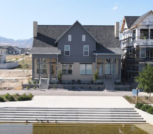 A charming two-story gray house in Coventry sits serenely by a small canal, where ducks glide peacefully on the water. Next door, another home is under construction, adding to the quaint charm of this inviting neighborhood.