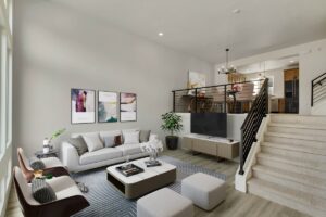 Modern living room with neutral tones, featuring a white sofa, coffee table, and armchairs. There are stairs leading to a mezzanine with a dining area and kitchen. Art pieces adorn the wall.