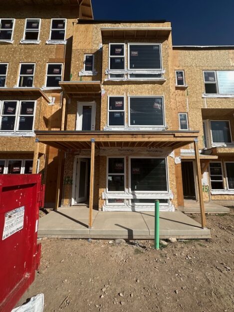 A three-story building under construction showcases exposed plywood and newly installed windows, with a red dumpster prominently placed in the foreground. It's reminiscent of the precision you’d expect at Major League 176.