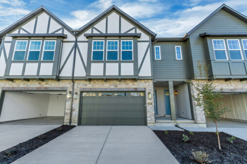 A modern townhouse with a double garage, stone and siding exterior, featuring multiple windows and a small tree in front.