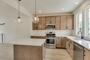 Modern kitchen with wooden cabinets, stainless steel appliances, island counter, and pendant lights, offering a tranquil retreat just steps from Lake West.