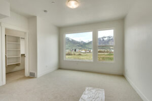 The empty room features a large window offering a Grand Slam of scenic mountain and lake views. It boasts beige carpet and an open door leading to a walk-in closet, perfectly positioned on the lake's west side.