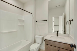 A minimalist bathroom featuring a bathtub, toilet, and vanity with a large mirror and sleek fixtures offers tranquility akin to a serene lake.