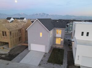 Aerial view of a suburban neighborhood with a gray two-story house, a partially constructed home on the left, and a mountain range in the background.