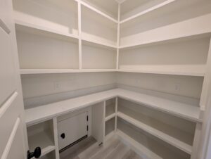 Empty white pantry with built-in shelves and corner countertop.