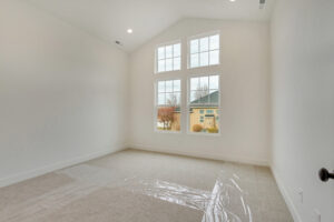 Empty room with beige carpet, vaulted ceiling, and large windows framing a view of houses and trees outside—like an issue #16 scene.