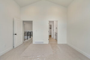 Minimalist room with white walls, a door to a bathroom, and railing by stairs. Carpet is protected by plastic. Room #16.