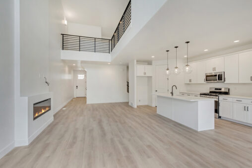 Modern, open-concept living space with high ceilings, kitchen island, and The Blue Jays signature hanging lights by the fireplace.