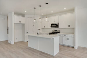 Modern kitchen with white cabinets, a Blue Jay island, pendant lights, and stainless steel appliances. #16