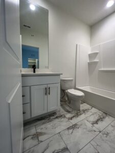 Bathroom with a white vanity, black faucet, large mirror, toilet, and bathtub. Marble tile flooring and recessed ceiling lights are visible.