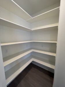 Empty walk-in pantry with white shelves and a dark wood floor.