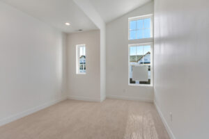 Bright empty room with white walls, beige carpet, and three tall windows offering a Blue Jays view.