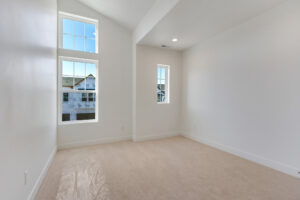 Empty white room with carpeted floor, three large windows showcasing partially constructed buildings and a passing Blue Jay.