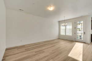 Minimalist empty room with wooden floor, white walls, a ceiling light, and a windowed door letting in sunlight.