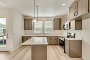 Modern kitchen with light wood cabinets, island, stainless steel appliances, and pendant lights.