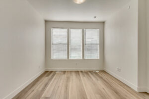 Minimalist room with wooden flooring and three large windows with blinds, letting in natural light.