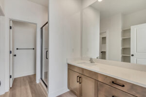 Modern bathroom with a large mirror, wooden vanity, glass shower, and white walls.